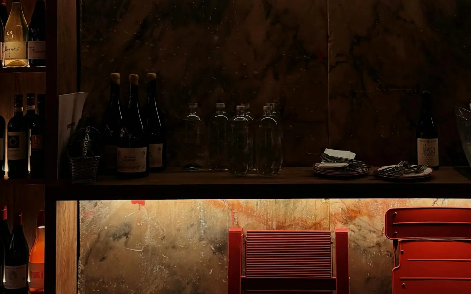 Warm, candlelit neighborhood wine bar with shelves of bottles, a cozy bar top and inviting golden light